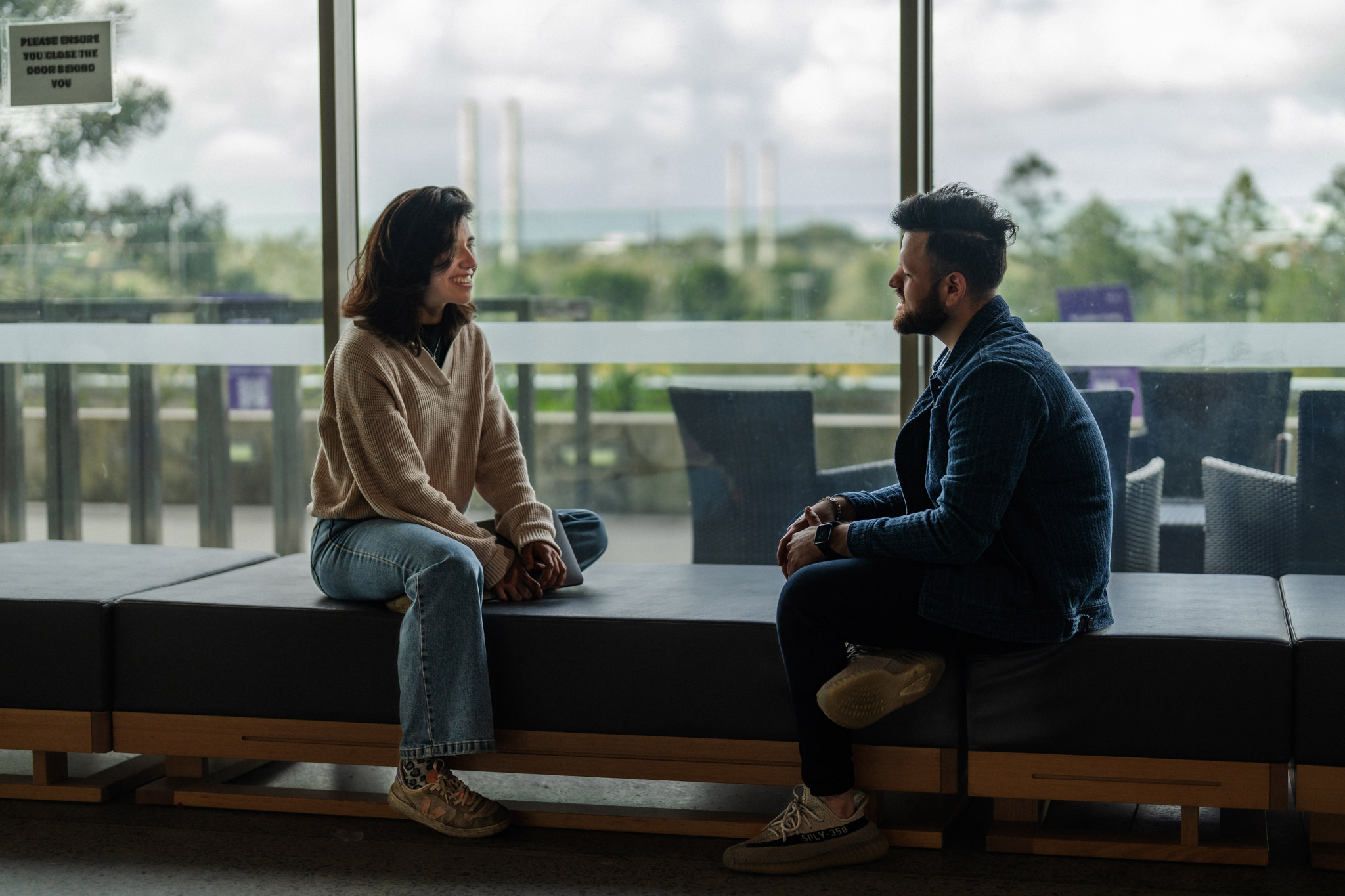 A female and a male student sitting near a window discussing study. 
