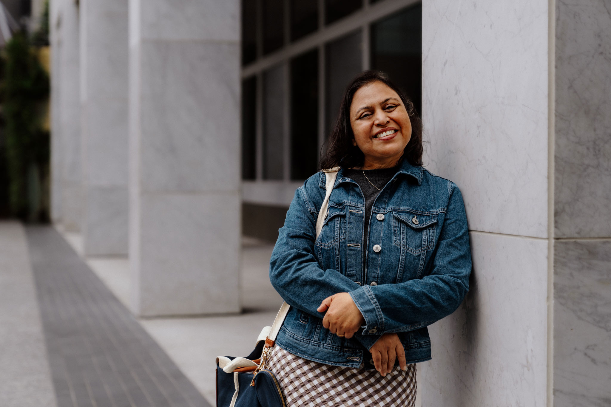 Female student leaning against a wall, smiling. 