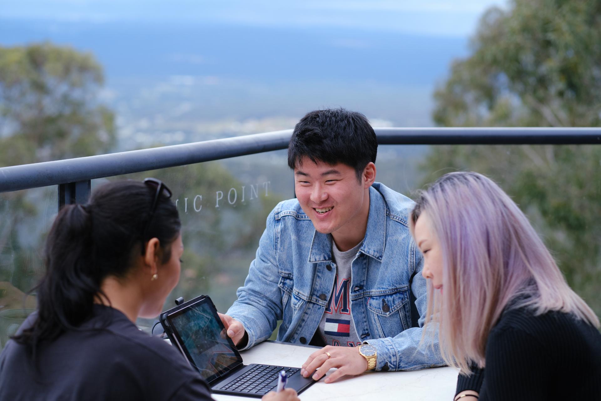 Three students sitting together looking at a laptop.